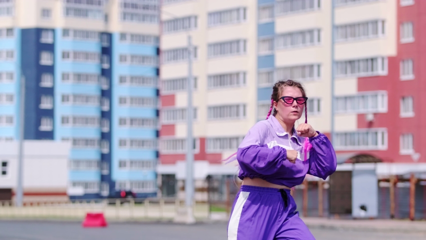 Young woman with colored pigtails dancing hip hop outdoorss, jumping and looking at the camera. Slow motion