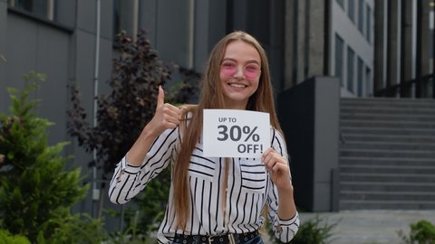 Happy smiling girl showing Up To 30 percent Off inscriptions signs, rejoicing good discounts, low prices for online shopping sales. Black Friday concept. Supermarket, mall on background. 6k downscale