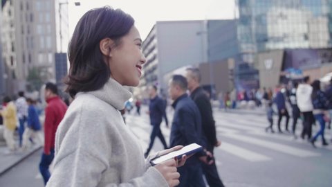 side view slow motion of one young asian woman walking across the urban street using mobile phone