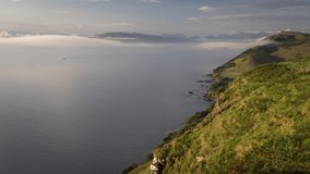 View of low clouds forming and rolling over sea and coastline during early morning on the Isle of Skye, Scotland. 4k time lapse video