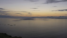 View of low clouds forming and rolling over sea and coastline during sunrise in Scotland. Sun rising behind the clouds and colors the sea in orange. 4k time lapse video