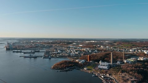 Slow descending aerial drone view of industrial area in Gothenburg, Sweden, with Rya Forest Nature Reserve visible lower right behind chimney