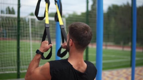 Caucasian sportsman doing pull ups exercise using fit belt to force strenth of workout outdoors