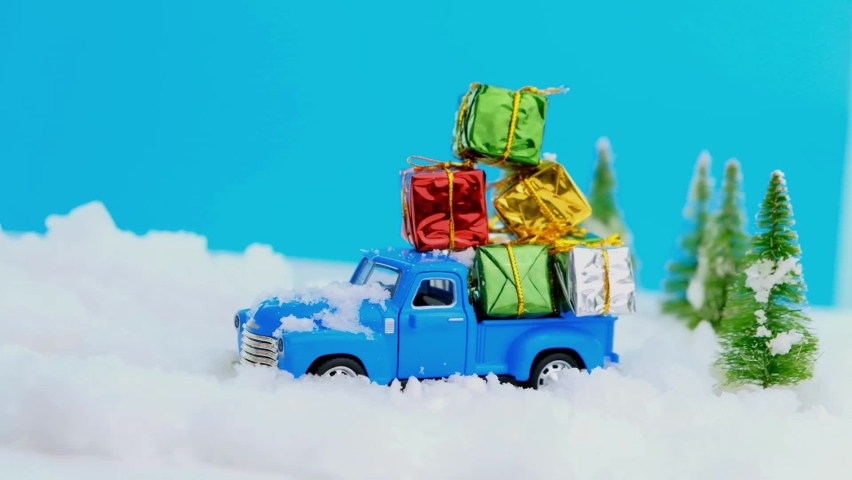 Christmas and New Year greeting card with gift delivery thuck goes on winter road in snow Xmas eve. Vintage blue truck carrying many gifts through the snowy forest. Christmas and holiday concept
