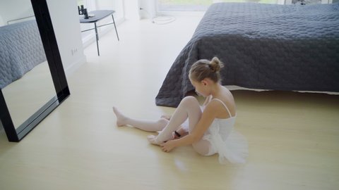 Girl (8-9) wearing ballerina dress putting on ballet slippers on floor in bedroom / Denmark