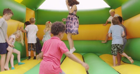 Children (6-7, 8-9, 10-11, 12-13) jumping in bouncy castle in garden / Dinton, Wiltshire, UK