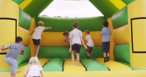 Children (6-7, 8-9, 10-11, 12-13) jumping in bouncy castle in garden / Dinton, Wiltshire, UK