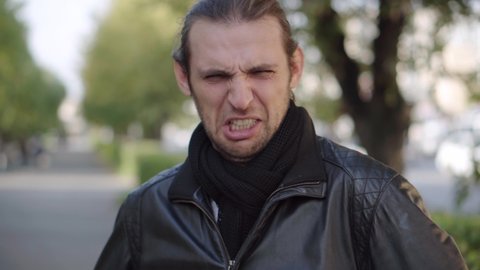 Young man in black jacket expressing disgust and disapproval with negative facial expressions outdoors. Facial expression.