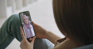 Female using medical app on smartphone consulting with Arab Muslim woman in hijab doctor via video conference. Female using online chat to talk with family therapist and pandemic of coronavirus.