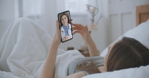 Woman checks possible symptoms with professional physician, using online video chat. Young girl sick at home using smartphone to talk to her doctor via video conference medical app.