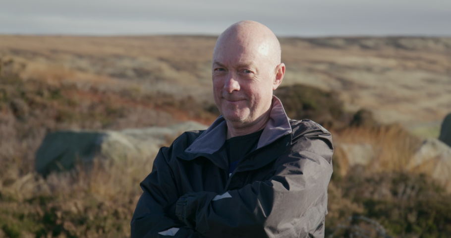 Portrait of smiling senior man in landscape / Yorkshire Moors, Yorkshire, UK
