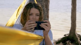 Video of brunette woman with her mobile phone relaxing on hammock.
