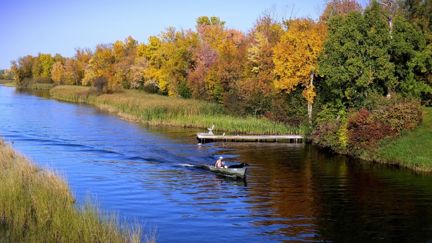 The beautiful Mississippi River in Bemidji, Minnesota with a small boat carrying a man and two black lab dogs on the blue water and autumn colors in the trees along the shoreline. Slow motion clip.