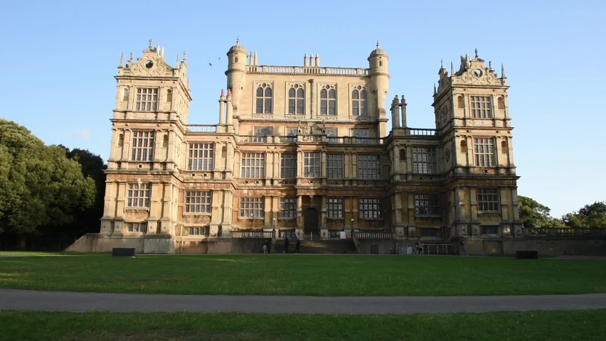 A view of the historic Wollaton Hall on the grounds of Wollaton Park in Nottingham. People walking at Wollaton Hall Park in Nottingham on a sunny day with green field.
