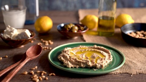 Long clip of beautiful setting of middle eastern food as hand comes in a spreads hummus onto a plate, pours olive oil and sprinkles paprika.