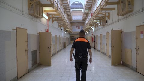 Barcelona / Spain 12 09 2020: Following shot of a prison supervisor in black and orange suite with handcuffs, gloves and a baton bypassing the corridor of a jail.