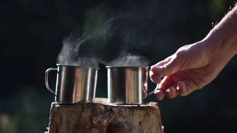 steam comes from two cups of hot coffee, a man's hand picks up one of them