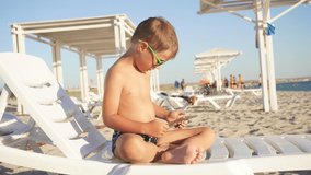 little boy uses a tablet on a chaise longue during the summer holidays, children learn on gadgets.