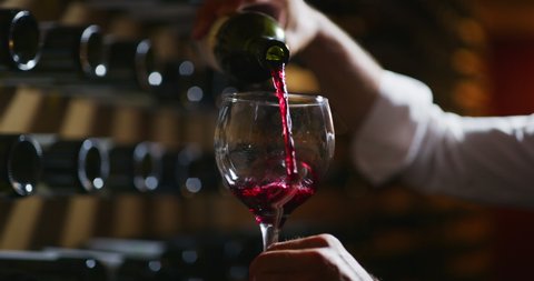 Close up shot winemaker or sommelier is pouring red wine in transparent glass for tasting a flavor and checking a quality  in a wine cellar.