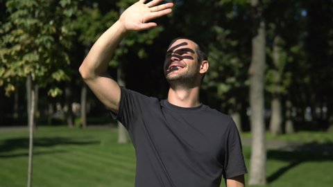 A young attractive guy squints at the sun and covers his face with his hand. Slow motion portrait of a young guy who smiles broadly and squints at the sun.
