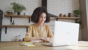 Happy african american young woman looking at computer screen, waving hello. Pleasant attractive mixed race female professional holding video call with client.