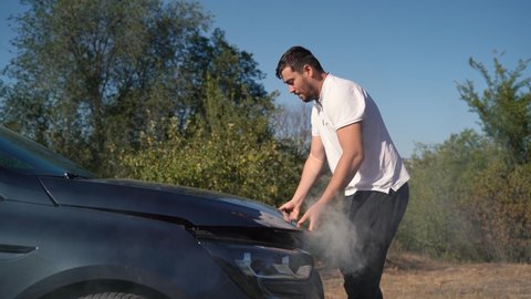  smoke under the hood of a car stuck on the roadside. A man opening it and becoming desperate because his vehicle broke down in the middle of nowhere.