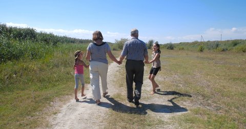 Active happy and healthy elderly European couple on a walk with their two granddaughters enjoying beautiful landscape. Tracking shot, rear view. slow motion 4k 50 fps