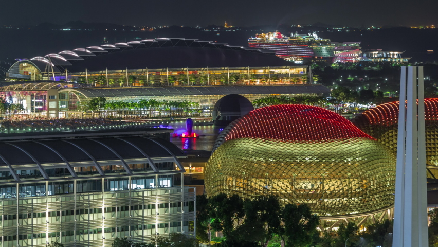 Beautiful laser and musical fountain show at the Marina Bay Sands waterfront in Singapore aerial night timelapse. Esplanade theatre illuminated roof. Boats floating around