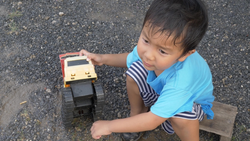 4K Asian child boy playing car truck toy in mud water outdoor. Happy kid enjoy in relaxing day, learning concept.