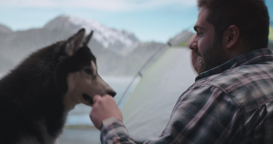 Hispanic male playing with his dog while resting near mountain lake campsite