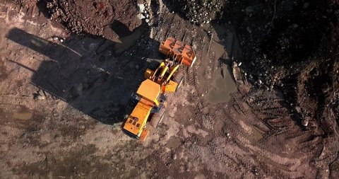 Large powerful yellow mining wheel operating loader lifts brown dirt on ground in Yukon, Canada, directly above aerial circle