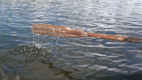 Wooden oar sweeping into rippling water on lake, slow motion shot