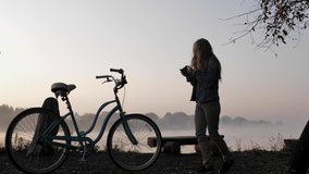 A woman films a vintage bicycle on her smartphone beside a foggy lake at dawn. High quality 4k footage