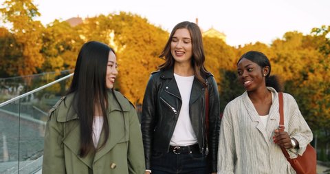 Mixed-races young women, best friends walking at city street and talking. Multi ethnic females strolling outdoor in park, gossiping and sharing secrets. Video Stok