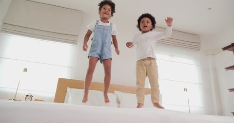 Little boy and girl jumping on bed at bedroom together. They jumping with funny emotion at home. Slow motion shot.