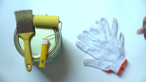 Close up of man hand putting brush, paint can, roller and gloves on white background. Painting equipment. Concept of DIY, paint, home, renovation, work, decoration, idea, home and hobby.