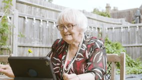 Elderly Woman talking on skype on a tablet device laughing in the garden day