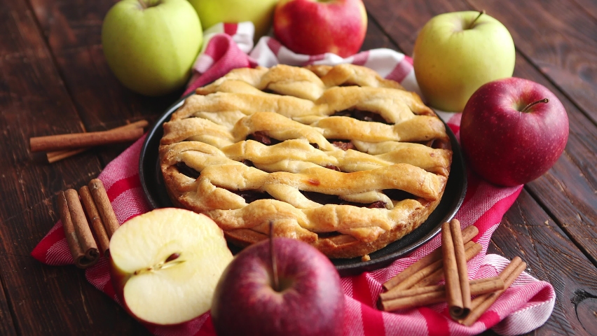 Homemade pastry apple pie with bakery products on dark rusty wooden kitchen table red and green apples and cinnamon. Traditional american dessert. Flat lay food background. Top view | Shutterstock HD Video #1059482564