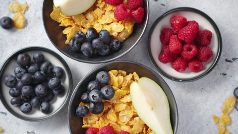 Healthy breakfast for two is served. Golden cornflakes with fresh fruits of raspberries, blueberries and pear in two ceramic bowls. Placed on stone background.