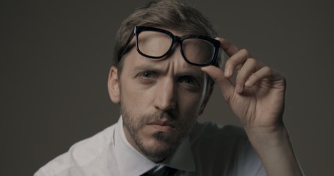 Man staring at camera and holding glasses, he is confused and has vision problems