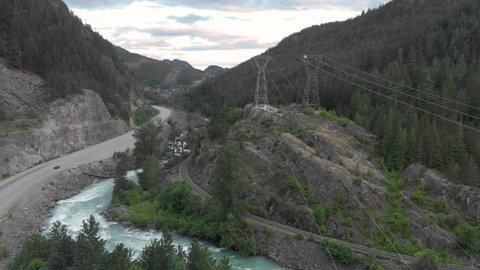 Aerial view of a mountain river with high tension power lines next to the sea to sky highway. 24FPS 4K.