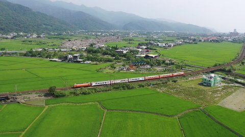 Aerial view of a Chu-Kuang Express train traveling thru a railway curve in the beautiful landscape of green rice fields and distant mountains, in the countryside of Toucheng Township, Yilan, Taiwan