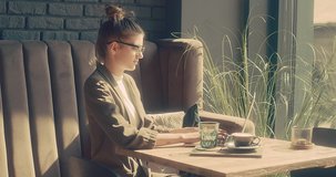 Woman working on notebook, sitting in cafe with coffee cup. Girl in glasses in pause, after work. Online chat with friends, long distance communication. Staying connected. 4K video Slow motion.