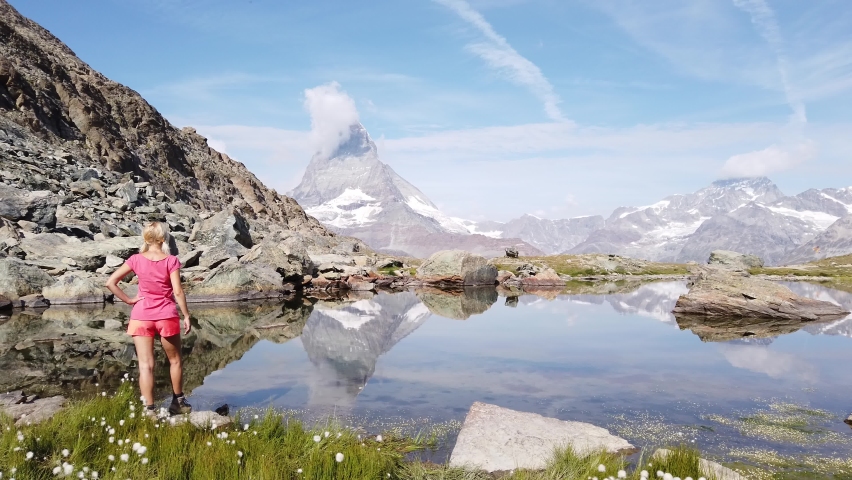 Tourist woman in meditation at Riffelsee Lake with Matterhorn reflected in its calm waters. Tourism in Zermatt, Swiss Alps, Valais, Switzerland. Riffelsee is located on Gornergrat Bahn cog railway.