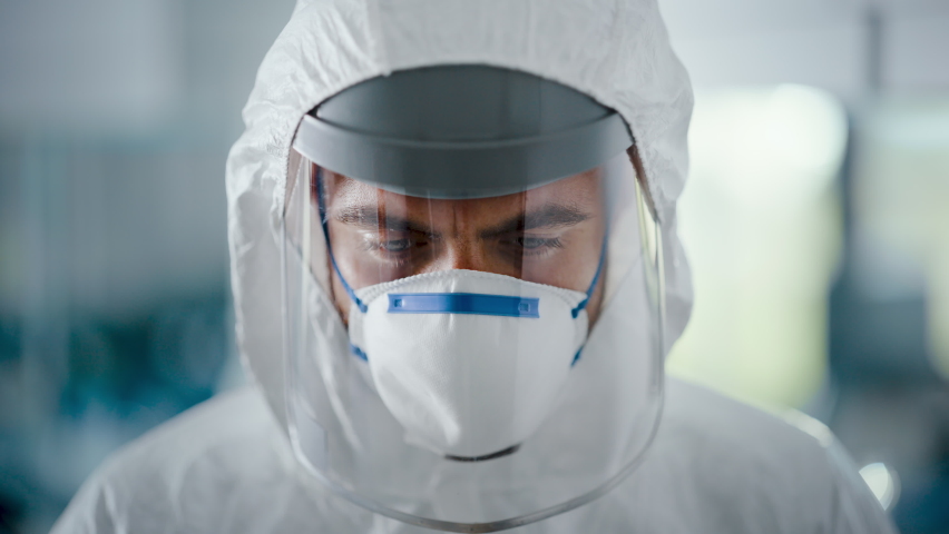 Dramatic Shot of Heroic and Overworked Medical Worker Wearing Coverall, Face Mask and Shield Looks Up at the Camera with His Piercing but Hopeful Eyes. Health Worker Fighting against Pandemic | Shutterstock HD Video #1059497927