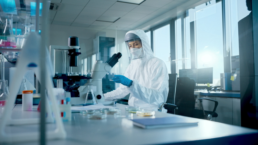 Beautiful Female Medical Scientist Wearing Coverall and Face Mask Using Micro Pipette while Working with Petri Dish. Vaccine, Drugs Research and Development Laboratory with Modern Equipment | Shutterstock HD Video #1059497933