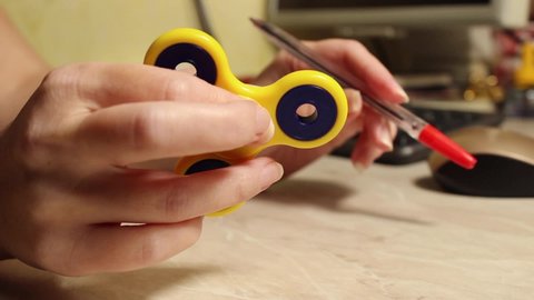 A yellow hand spinner spins in a woman's hand with a computer in the background. Close up.