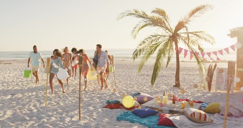 Front view of mixed race friends on holiday enjoying time together on a tropical beach at sundown, walking to the party site and smiling, in slow motion