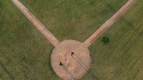 Overhead view of a baseball team playing a game outdoors on a baseball field at sundown on a sunny day, the hitter making a run and arriving back at home base as fielder catches ball, shot with drone