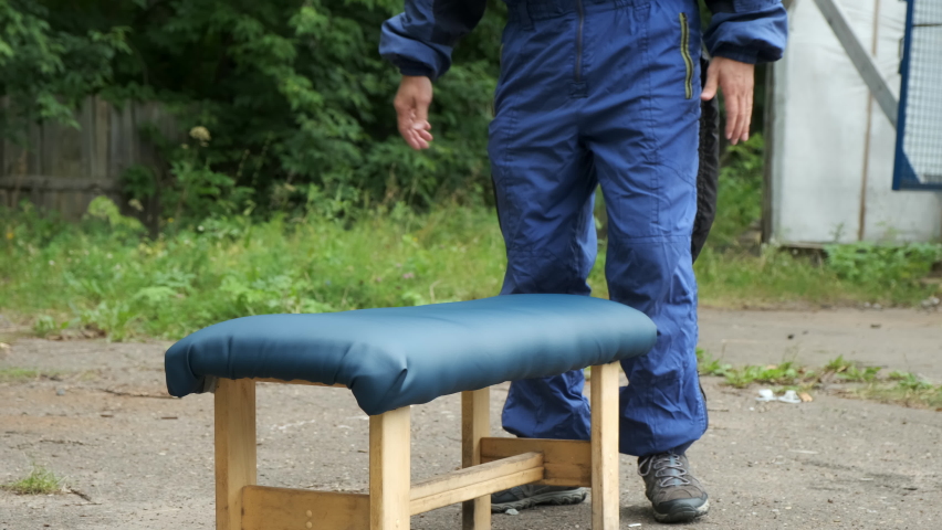 Man is training before flying in air tube in special costume lying on bench. Man instructor is explaining him right pose for flying near her outdoors. Preparing to aerodynamic tube.